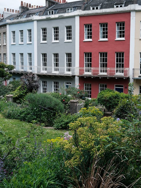 A city rooftop garden featuring a paved central pathway bordered by rectangular wooden planters filled with various plants, including succulents and small shrubs, with some showing fresh green foliage